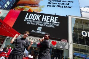 TFFJ alums Fiona C. and Najae S. posing in front of the #FlattenBigSoda ad in Times Square.